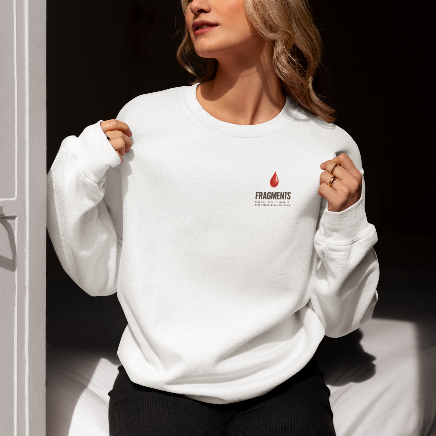 Vrouw draagt een witte sweatshirt met het "FRAGMENTS" logo en een rode vlamdruppel op de borst.